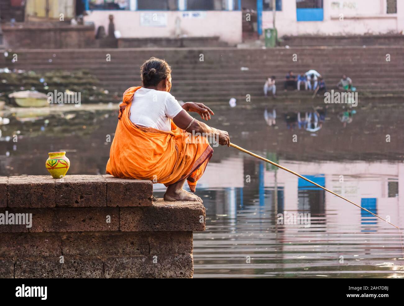 Bhubaneshwar, Orissa, Indien - 12. Februar 2018: Eine alte Frau fischt mit einem Angelpfahl, während sie auf einer Steinplattform auf dem alten Bindu Sagar l sitzt Stockfoto