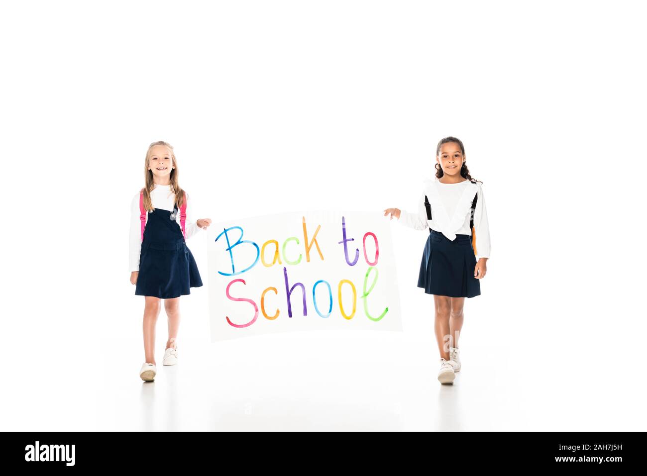 Volle Länge aussicht auf zwei multikulturelle Schülerinnen holding Plakette mit Inschrift zurück zur Schule beim Gehen auf weißem Hintergrund Stockfoto