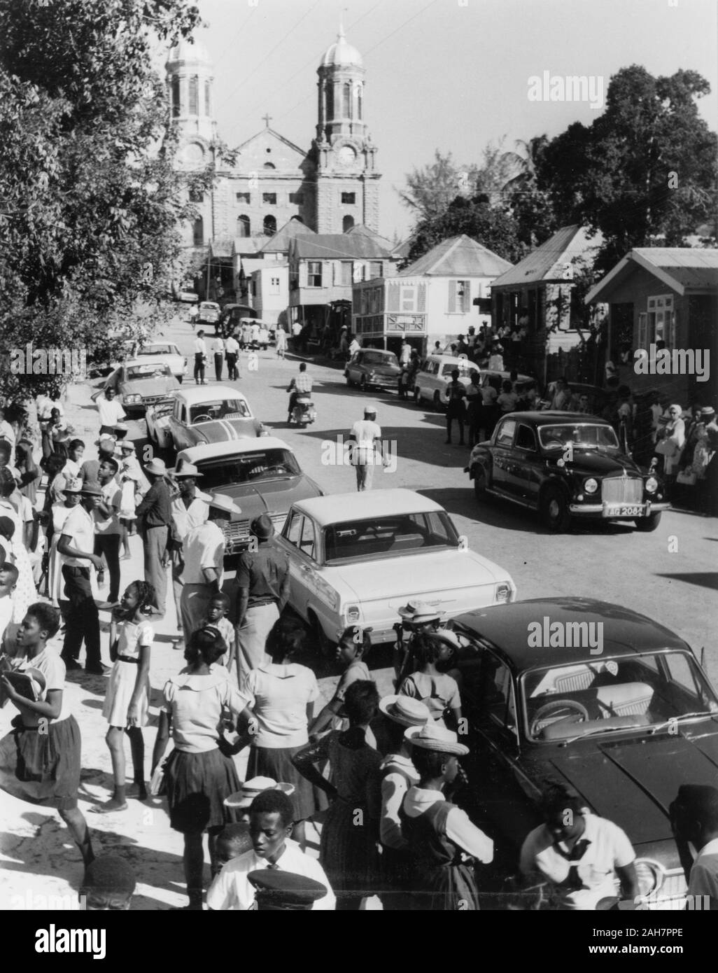 Antigua, Warten auf den Karneval zu starten. Werdende Menschenmassen versammeln sich auf der Hauptstraße in St John's, warten auf einen faschingszug zu beginnen. Die zwei weißen barocken Türme der Kathedrale von St. John's sind in der Ferne zu sehen. St. Johns, Antigua, 1965. Bildunterschrift lautet: DIE HAUPTSTRASSE IST BEREIT FÜR DIE PROZESSION, 1965. 2005/010/1/13/24. Stockfoto