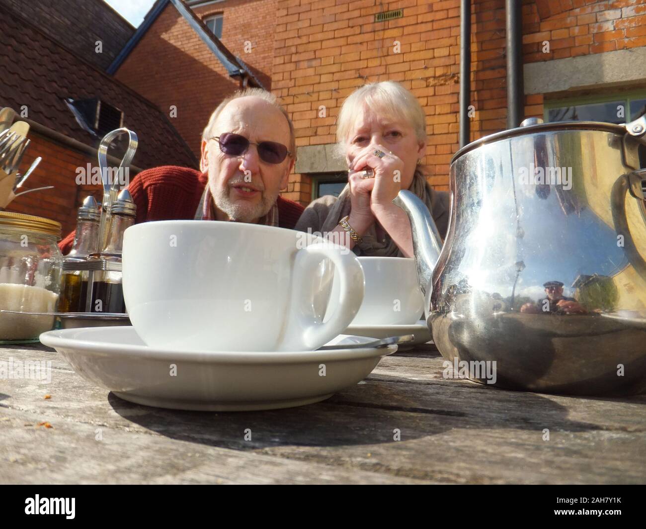 Ein paar Rentner reflektieren auf eine Tasse Kaffee in der Frühlingssonne. Glastonbury, Somerset, Großbritannien Stockfoto