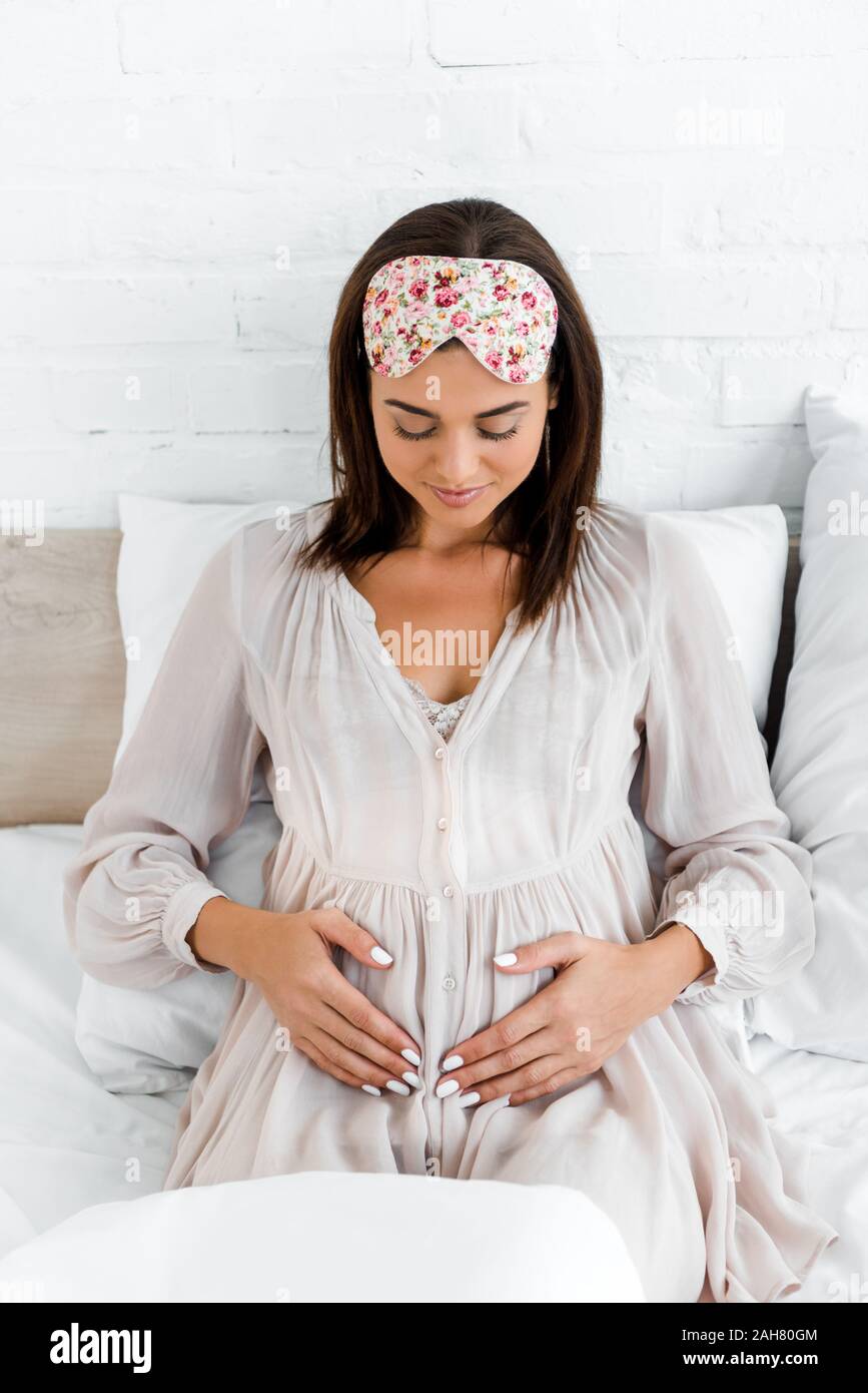 Schwangere Frau in Schlafmaske ihren Bauch berühren, während Sie im Bett lag, Stockfoto