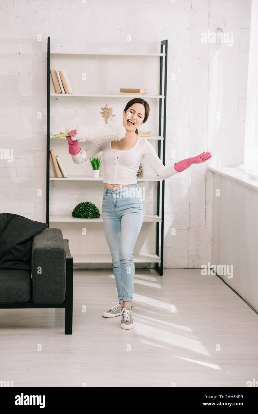 Gerne Hausfrau singen mit staubbürste beim Stehen in der Wohnzimmer Stockfoto