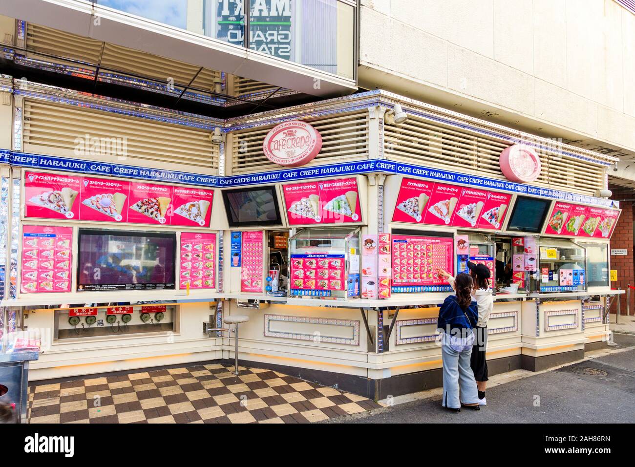 Zwei japanische junge Frauen wählen Takeaway Crepes von außen Menü Vorstand im Cafe Crepe Harajuku Laforet Strawberry House in Tokio. Stockfoto