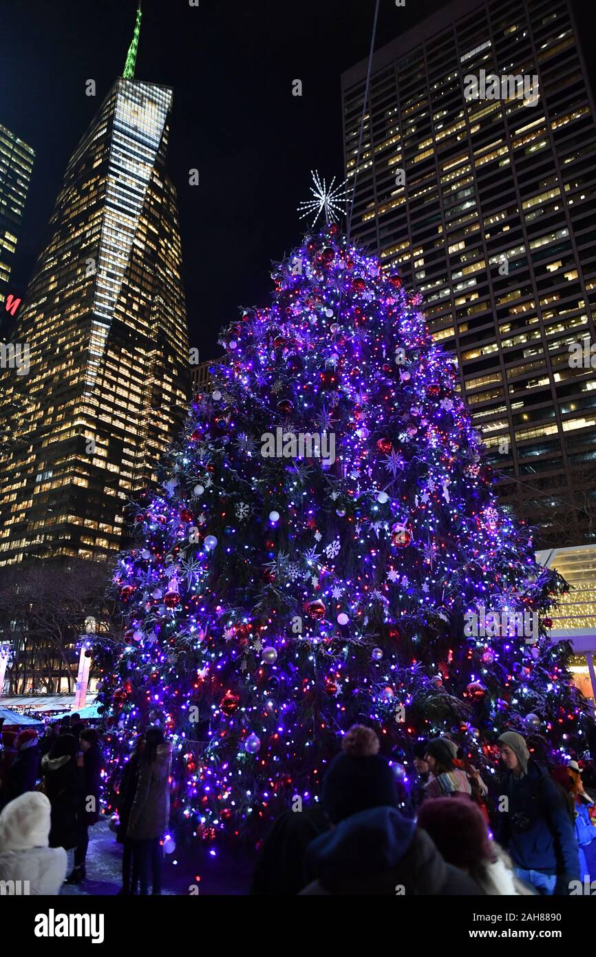 Ein Weihnachtsbaum erstrahlt über dem Winter Dorf und Urlaub Geschäfte im Bryant Park in New York. Stockfoto