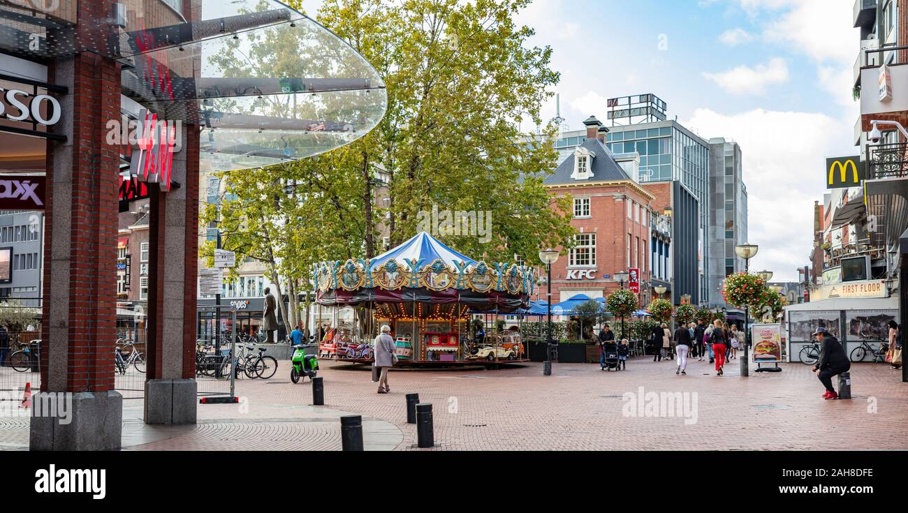 Eindhoven, Niederlande. Oktober 10, 2019. Retro Merry-go-round Spiel in einem gepflasterten Platz. Menschen gehen, während in den Läden auf der Suche. Gebäude Hintergrund Stockfoto