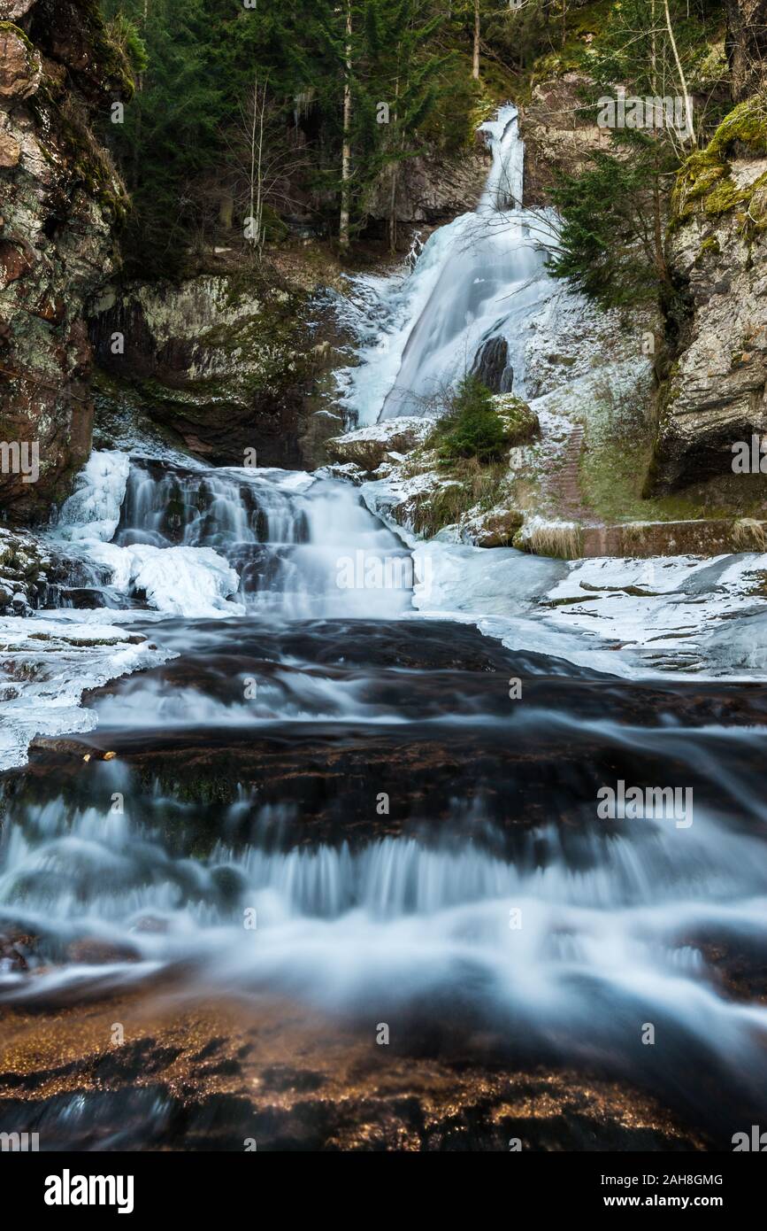 Niedriger Blick auf einen tiefgefrorenen, alpinen Wasserfall zwischen Felsen und aus Kiefernholz Stockfoto