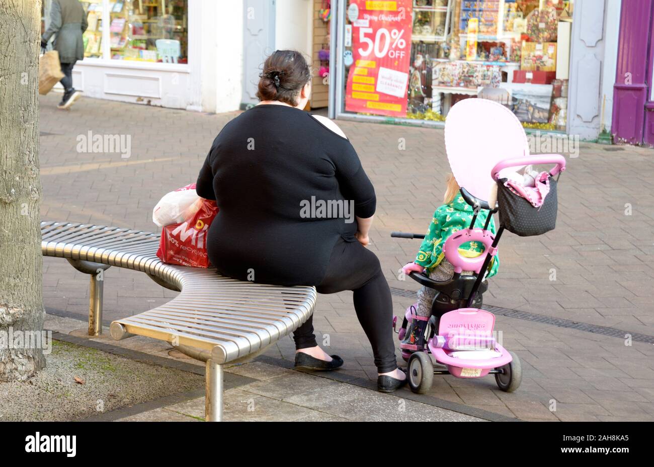 Sehr fette Dame, in schwarz, mit einem kleinen Kind in rosa Kinderwagen Stockfoto