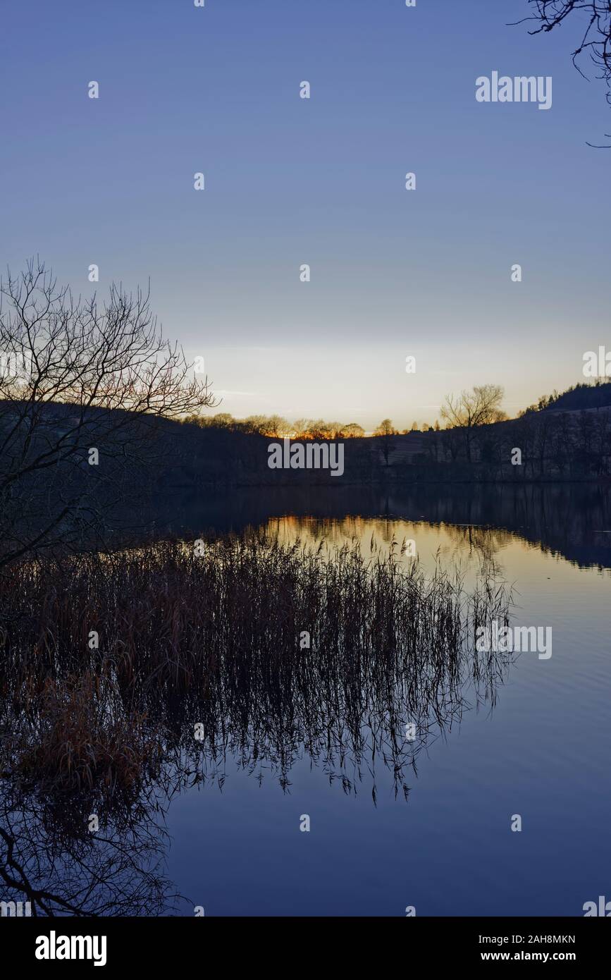 Schilfrohr und Reflexionen in den ruhigen Wassern der Clunie Loch in der Dämmerung auf einem kalten Weihnachtstag im Jahr 2019. Stockfoto