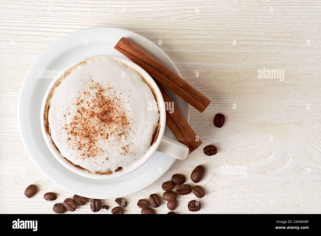 Tasse Cappuccino mit Kaffeebohnen und Zimtstangen auf Weiß Stockfoto