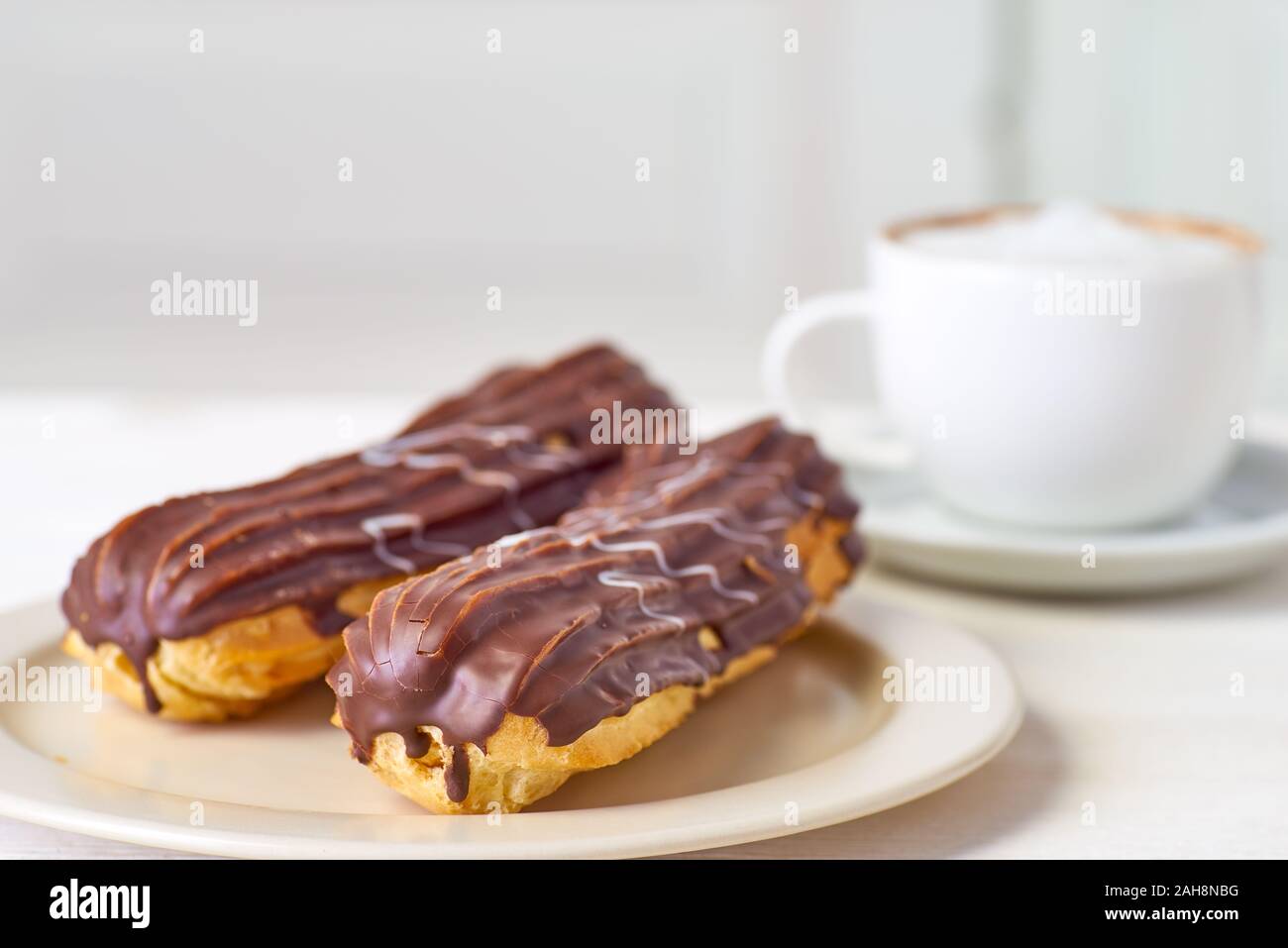 Teller mit zwei Eclairs und Tasse Kaffee auf weiße Holztisch Stockfoto