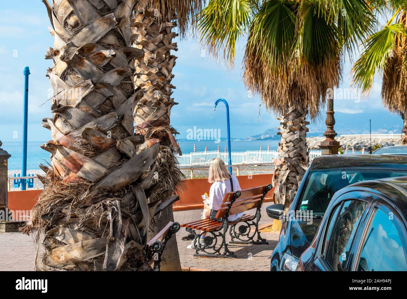 Nicht identifizierbarer Frau isst ihr Mittagessen auf einer Parkbank vor dem Mittelmeer an der Küste von Ventimiglia, Italien, an der Riviera. Stockfoto