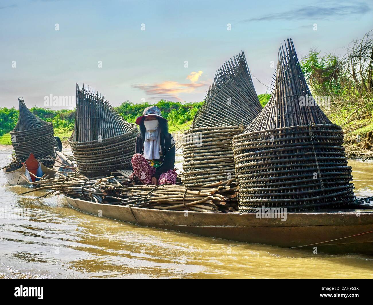 Ein kambodschanisches Frau sitzt in einem hölzernen Boot geschleppt wird ein Fluss. Das Boot ist mit hausgemachten Angeln trap gefüllt. Stockfoto