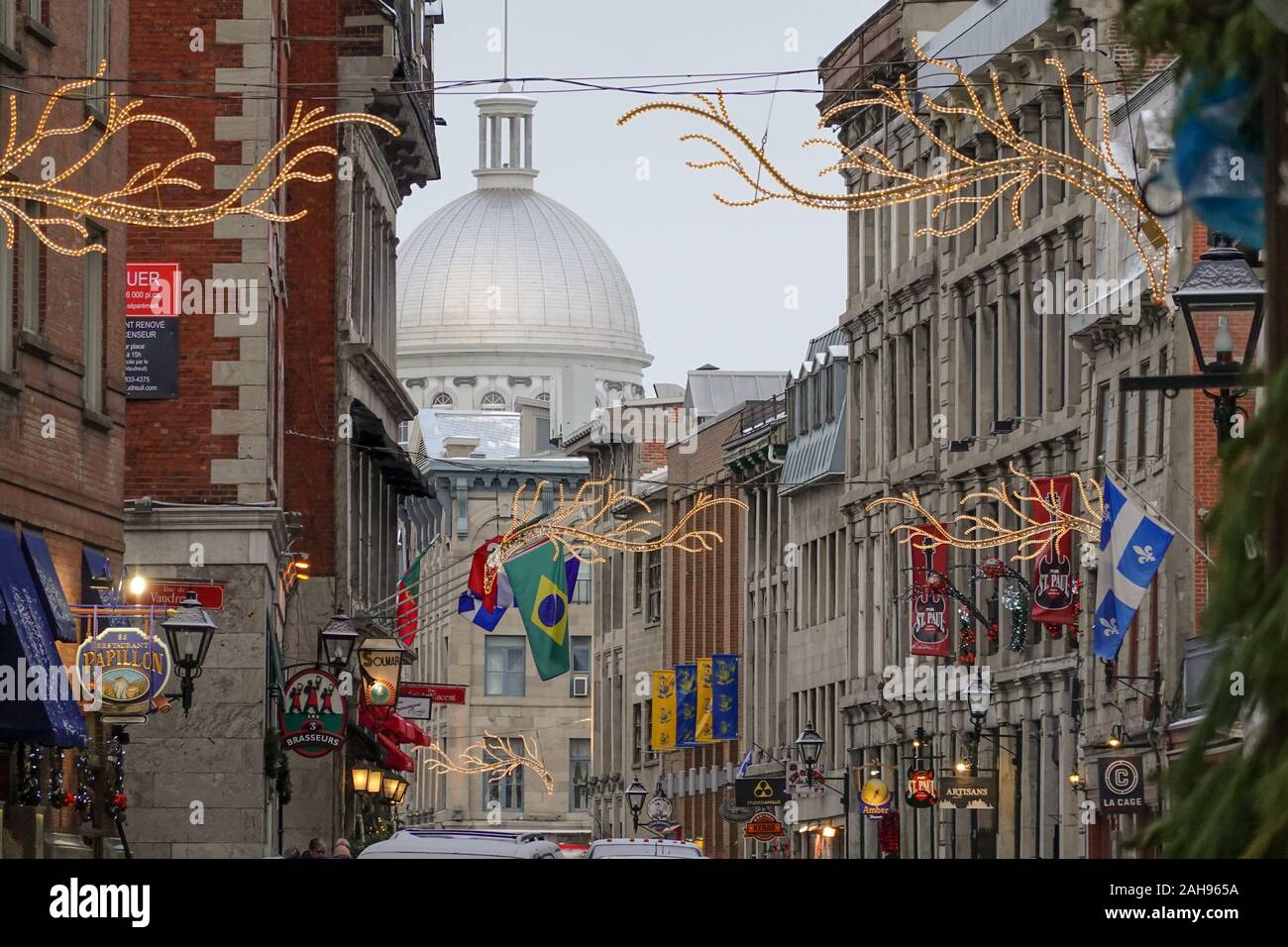 Blick auf die Straße im alten Hafen von Montreal, wo mehrere Nationen Flaggen quebecs brasiliens und die Kuppel der marken bonsecours mit aufgehellten Dekorationen zeigen Stockfoto