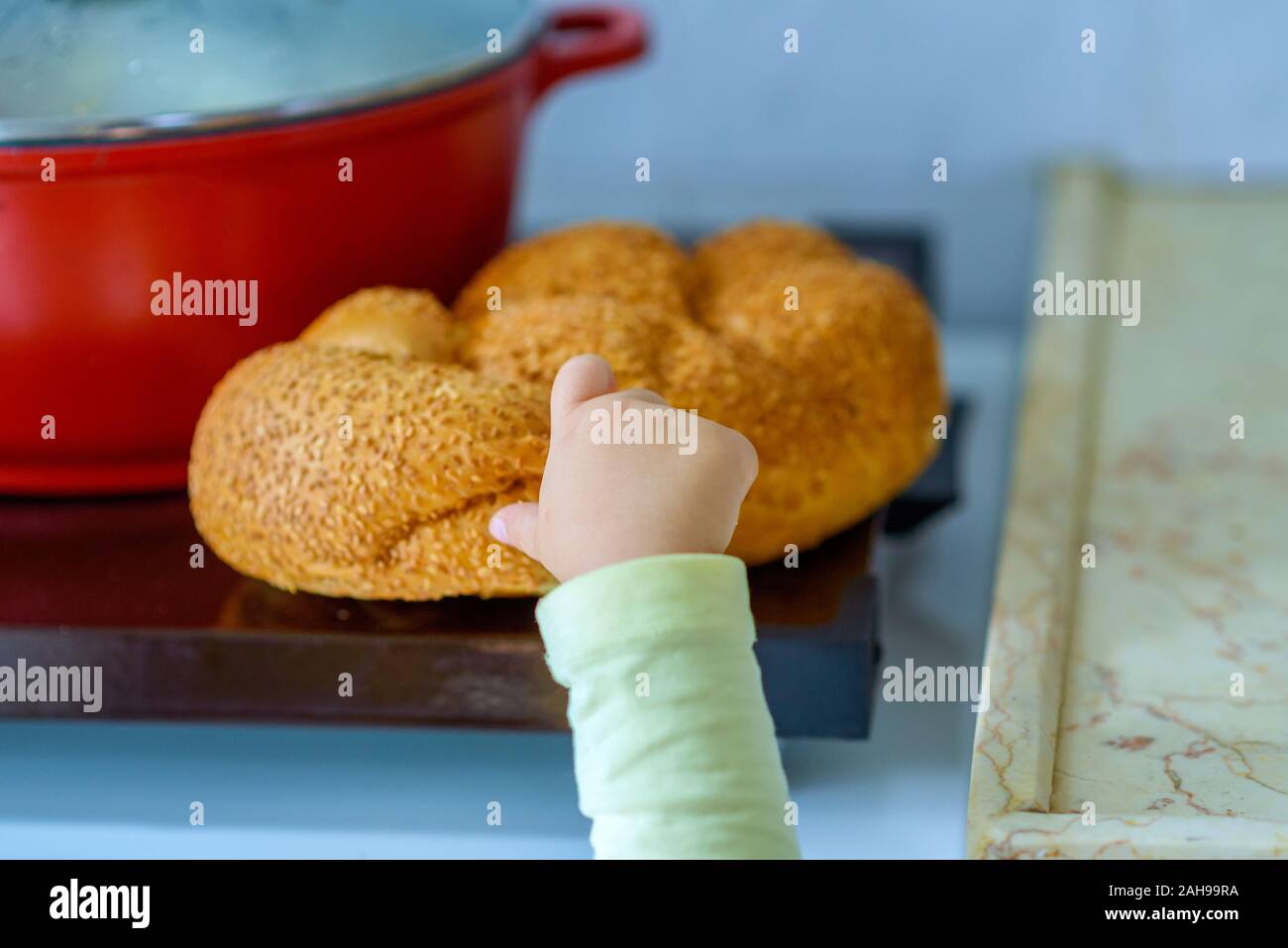 Die Hand eines hungrigen Kind halten und ein Stück Brechen des Brotes. Ein Kid's Hand reißt ein Stück challah. Heiße Platte für den Sabbat. Topf mit traditionellen Speisen und challah - spezielle Brot in der jüdischen Küche. Stockfoto