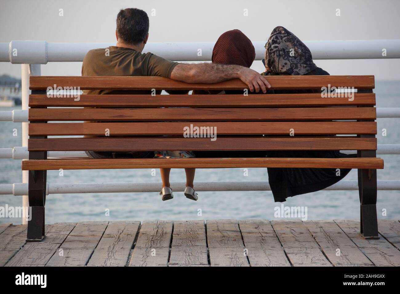Die iranische muslimische Familie genießt einen Blick auf das Meer über einer Terrasse neben einem Park. Vater, Mutter und Töchter haben als Familienzeit einen intimen Kreis geschlossen. Stockfoto