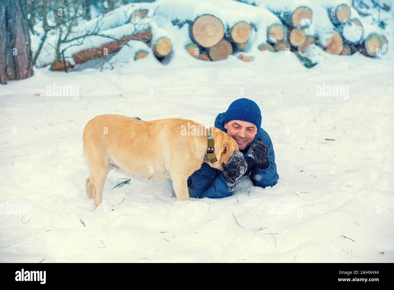 Ein Hund und Mensch sind die besten Freunde. Eine glücklich lächelnde Mann liegen auf dem Schnee im Winter. Der Mann spielt mit einem Labrador Retriever Hund Stockfoto