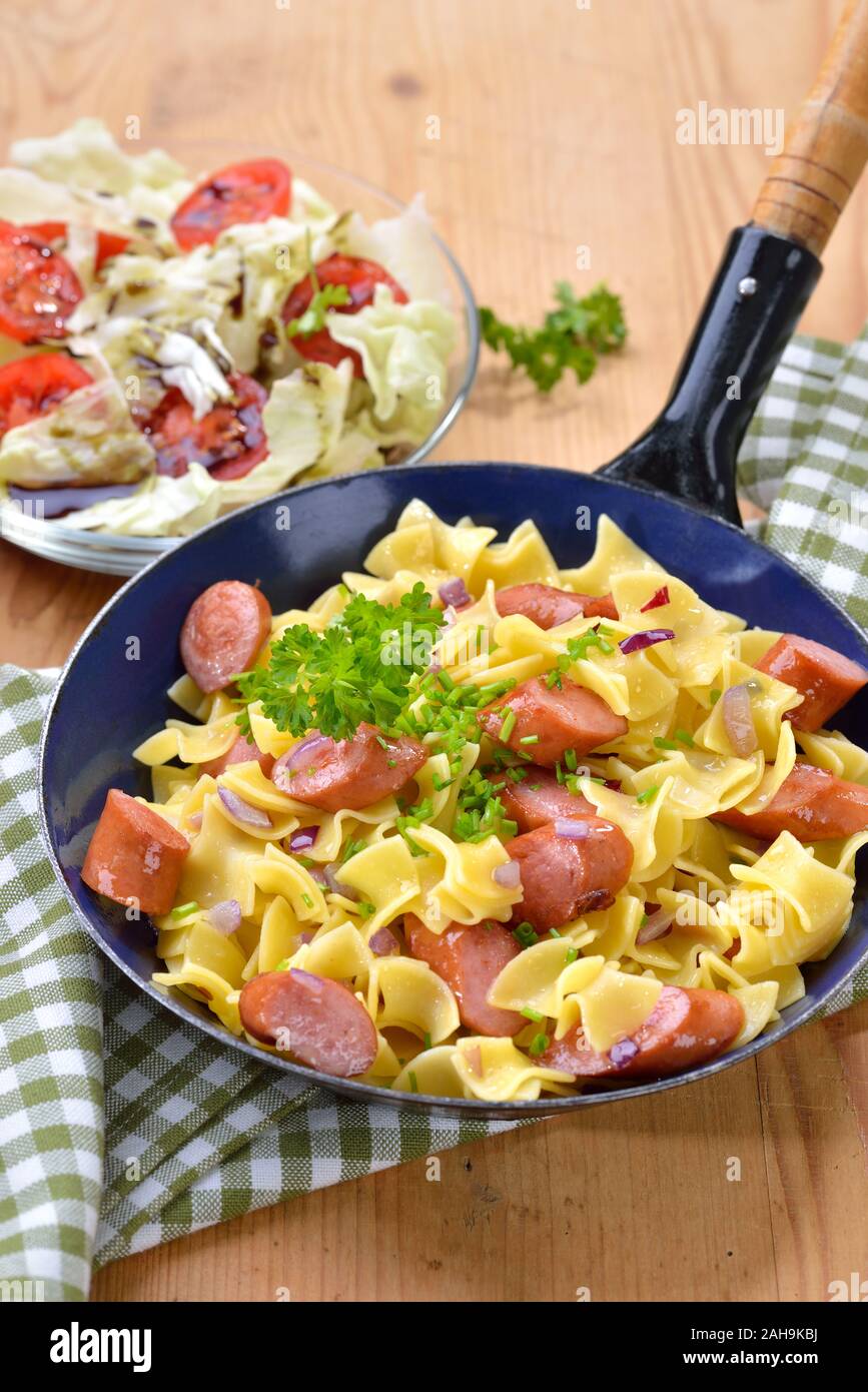 Österreichische Mahlzeit mit Pasta und würzigen Würstchen gebraten, so genannte Wurstfleckerl, serviert in einer Pfanne mit einem Beilagensalat mit Steirisches Kürbiskernöl Stockfoto