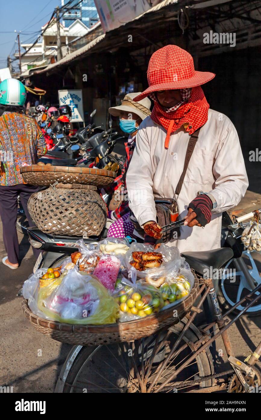 Eine Frau bereitet zu verkaufen Wüste, Obst und Donuts zu Ihrem Fahrrad geschnallt zu einem Straßenmarkt in Kampong Cham, Kambodscha.. Stockfoto