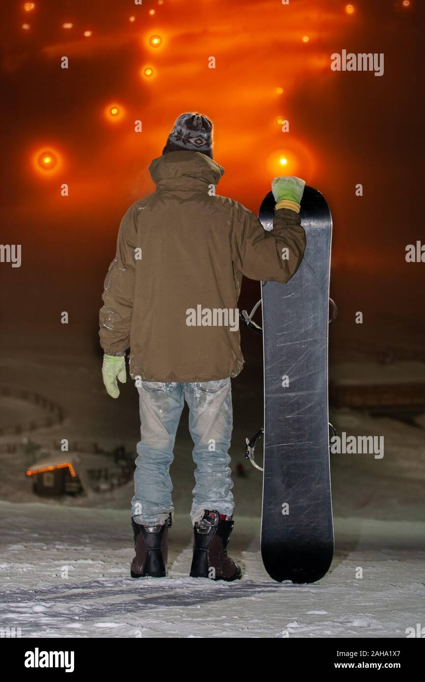 Ein junger Mann steht mit einem Skateboard auf dem Berg. Vorbereitung für den Abstieg vom Berg auf einem Skateboard. Nacht skateboarding. Stockfoto
