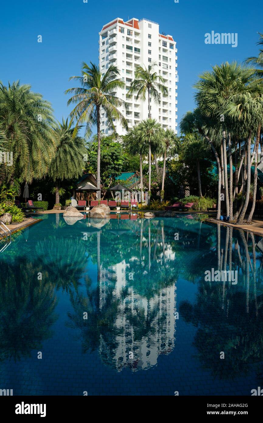 16.11.2019, Phuket, Thailand - Palmen am Pool des Mövenpick Resort & Spa Karon Beach Phuket. Der Wolkenkratzer im Hintergrund ist Stockfoto