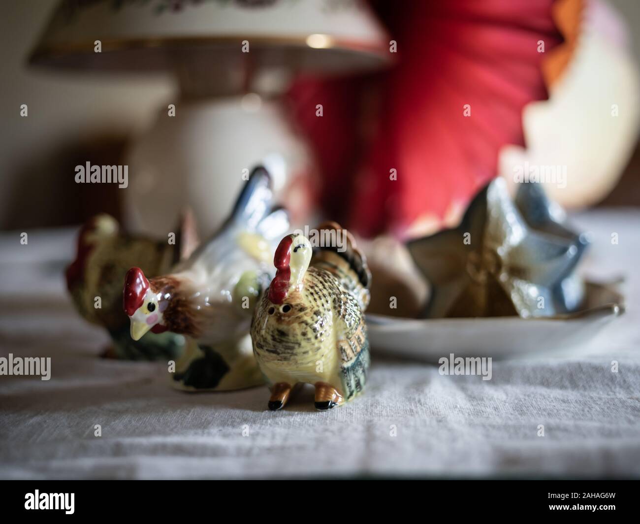 Truthahn und Huhn Salz und Pfefferstreuer auf einem weißen Tischtuch mit einer Lampe im Hintergrund. Stockfoto