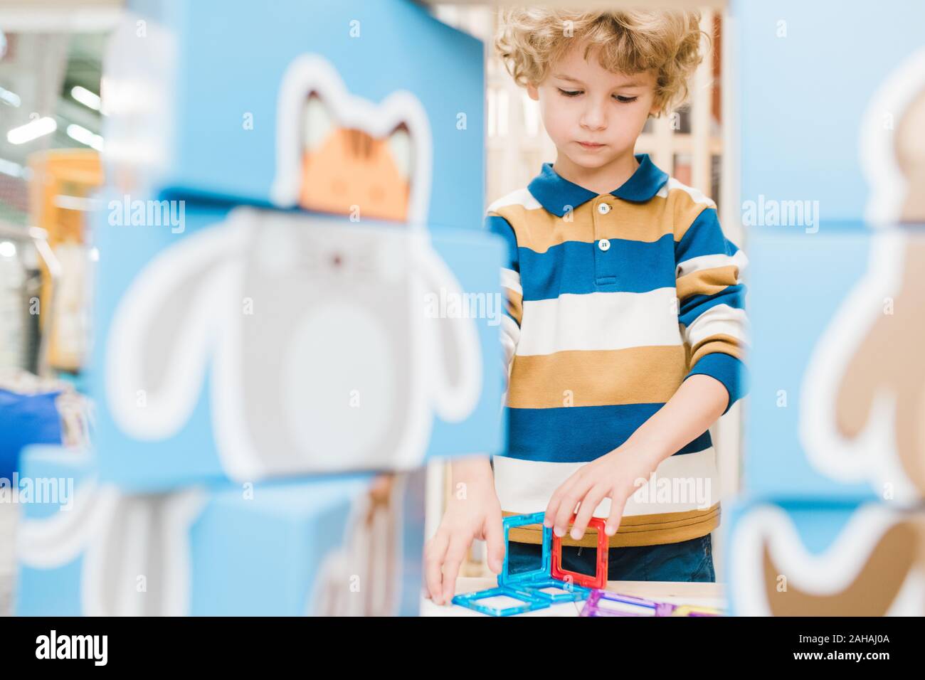 Adorable blonde Junge im gestreiften Hemd spielen multi-color Konstruktor Stockfoto