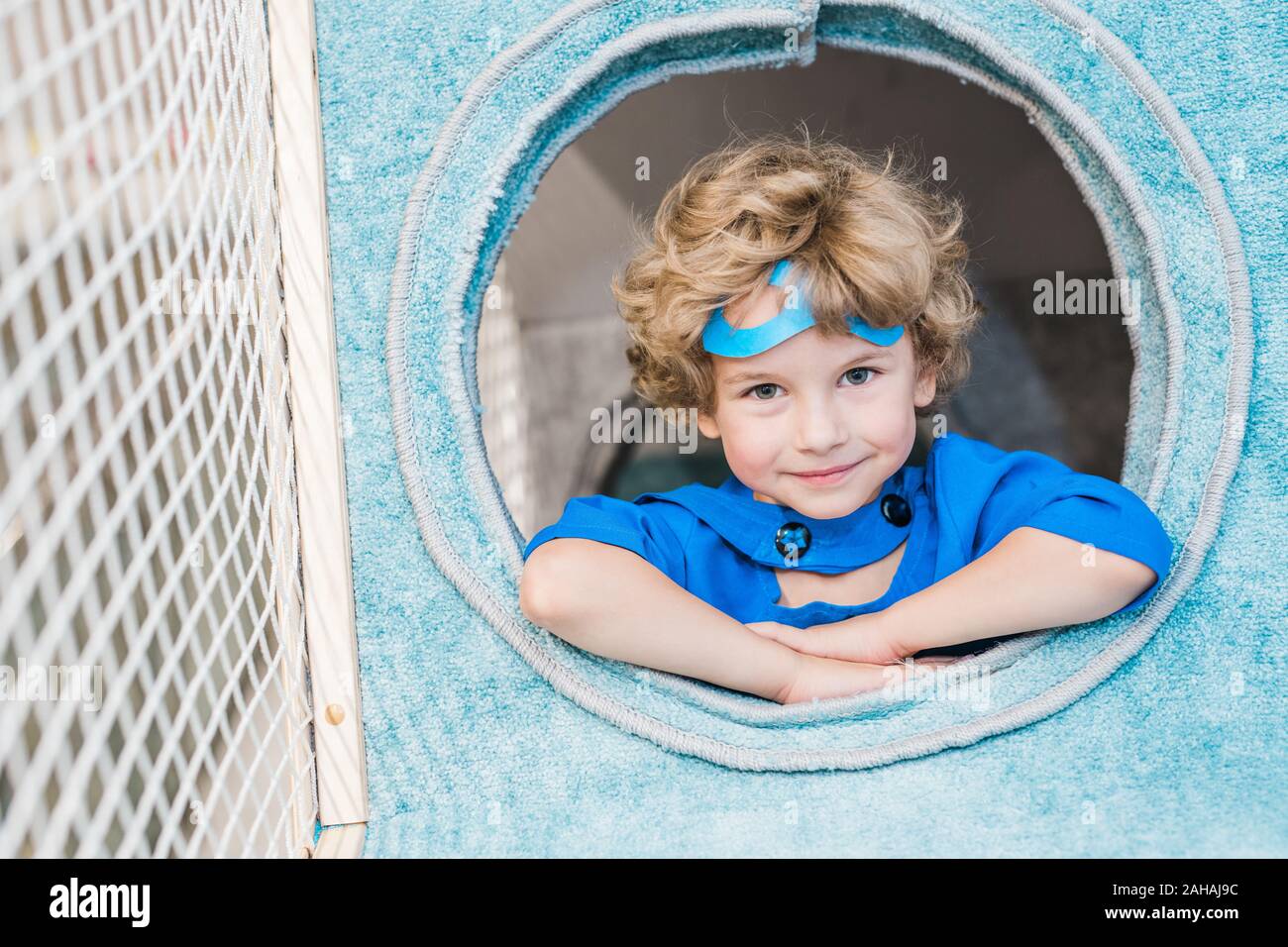 Blonde lockige kleine Junge im blauen Kostüm von Superman in runde Fenster Stockfoto