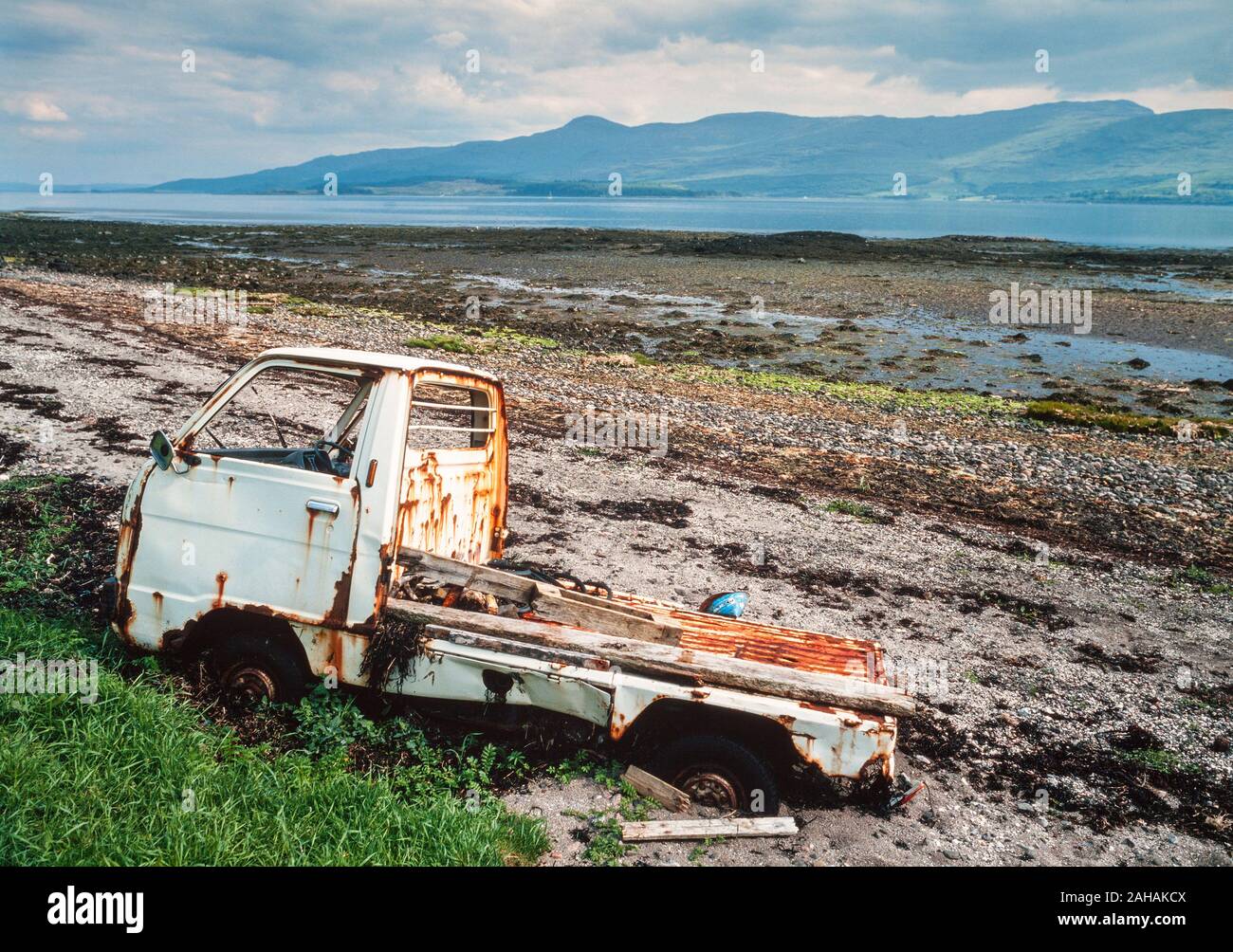 Küste Strand Verschmutzung, Westschottland, Großbritannien. Abgebrochene havarierten Fahrzeug auf Pebble Beach, Blick auf die Insel Mull. Stockfoto