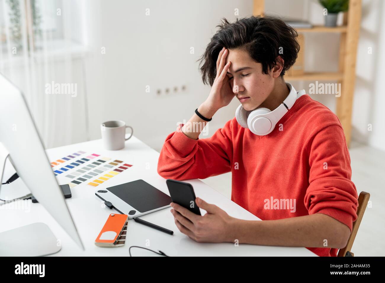 Müde Freiberufler berühren seinen Kopf, während Sie Ihr Smartphone in die Vorderseite des Computers Stockfoto