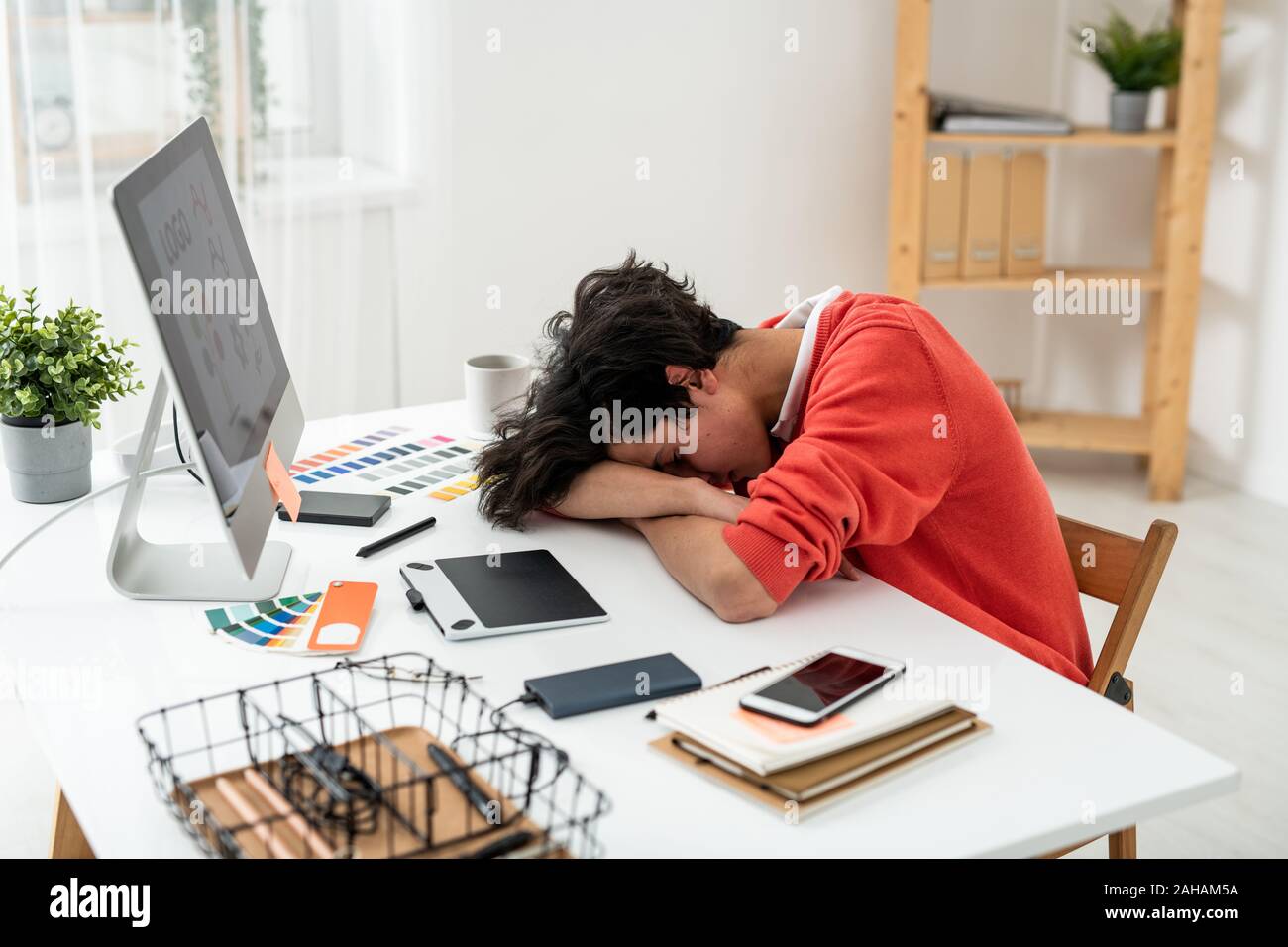 Erschöpft junge männliche Freelancer Nickerchen auf dem Schreibtisch vor dem Bildschirm Stockfoto