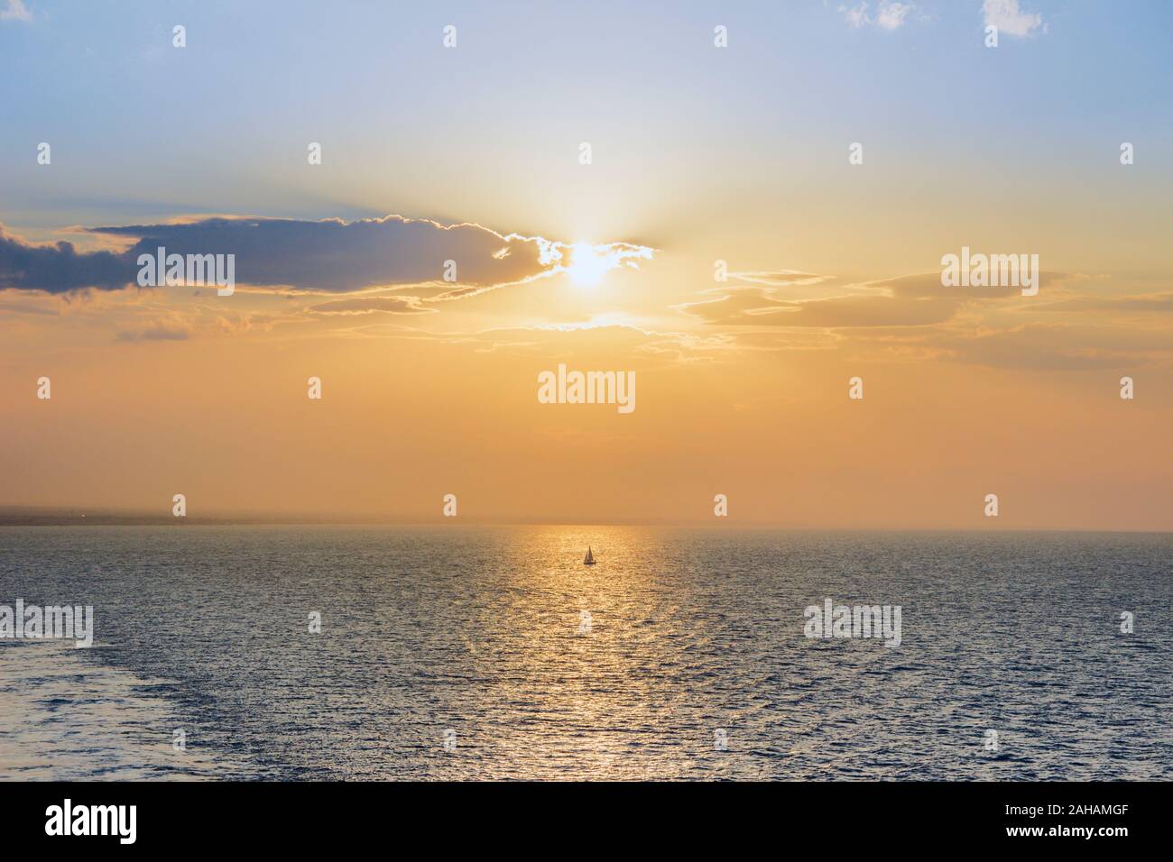 Segeln Bei Sonnenuntergang. Saisonale Bilder mit glänzendem Meer und segelboot über bewölktem Himmel und Sonne bei Sonnenuntergang Apulien Küste, Italien. Stockfoto
