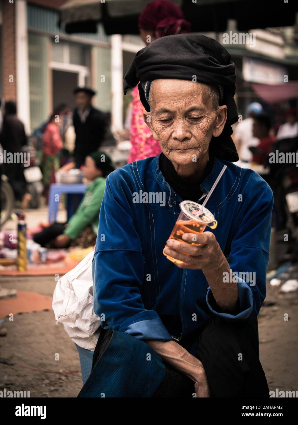 Ältere vietnamesische Dame der ethnischen Minderheit in traditioneller Kleidung mit Schale aus Kunststoff an der Dong Van Markt, Vietnam Stockfoto