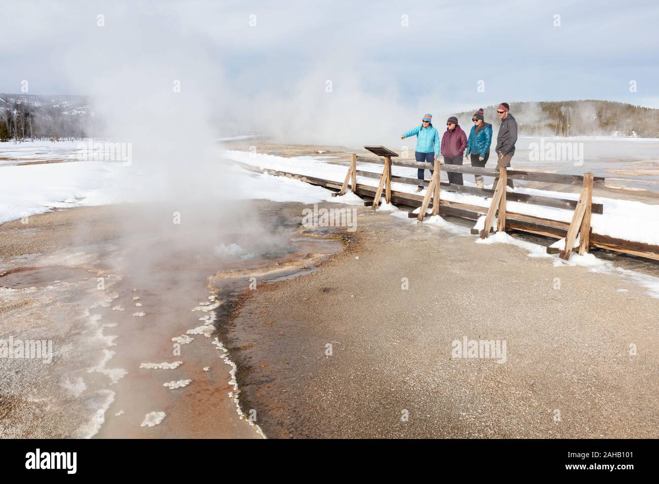 Eine Gruppe von Touristen beobachten Sie den Zimt Wasserspeier Geysir von der Promenade in der Upper Geyser Basin im Winter im Yellowstone Nationalpark Yellowstone, Wyoming. Yellowstone ist Heimat für die Hälfte der Welten Gesamtzahl der Geysire, mit Tausenden von heißen Quellen, und etwa 300 bis 500 Geysire. Stockfoto