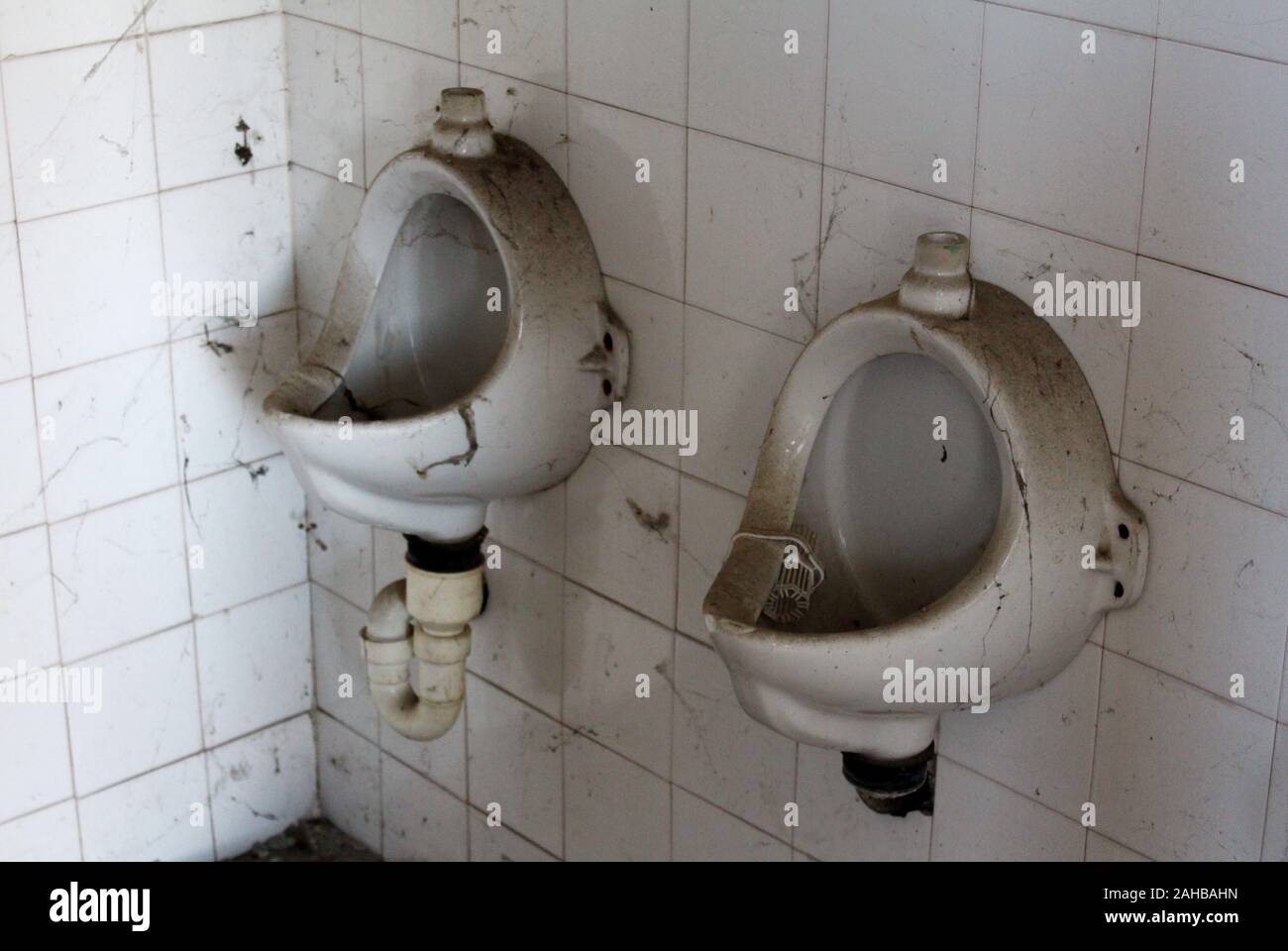 Zwei Vintage Retro alte getrennt Urinale bedeckt mit Staub und Cobweb auf weißen Fliesen an verlassenen militärischen Komplex, der auf warmen und sonnigen montiert Stockfoto