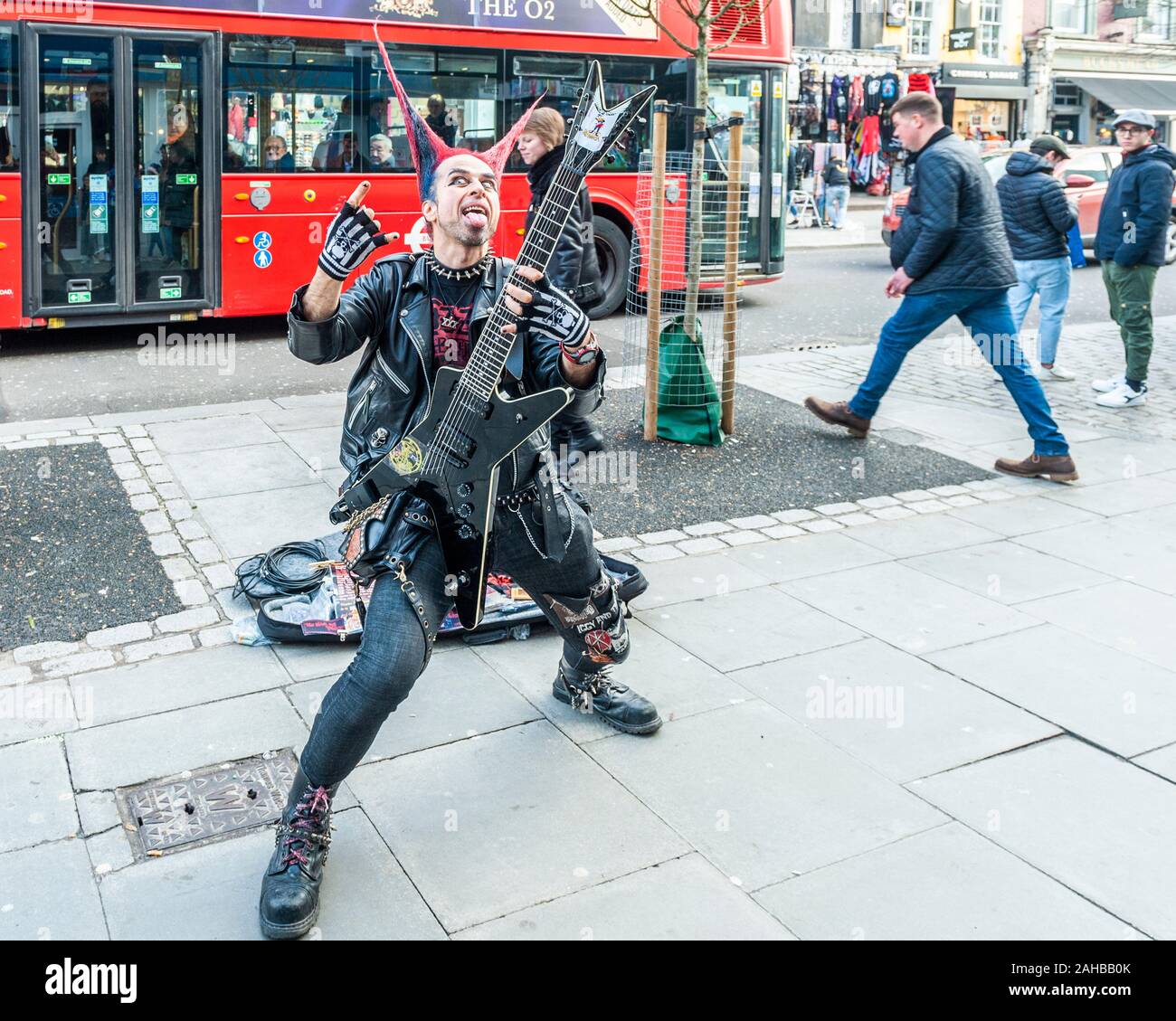 Mann in Punk-Rocker-Kleidung mit Stachelhaar und einer Gitarrenpose für Touristenbilder an der Camden High Street, Camden, London, Großbritannien. Stockfoto