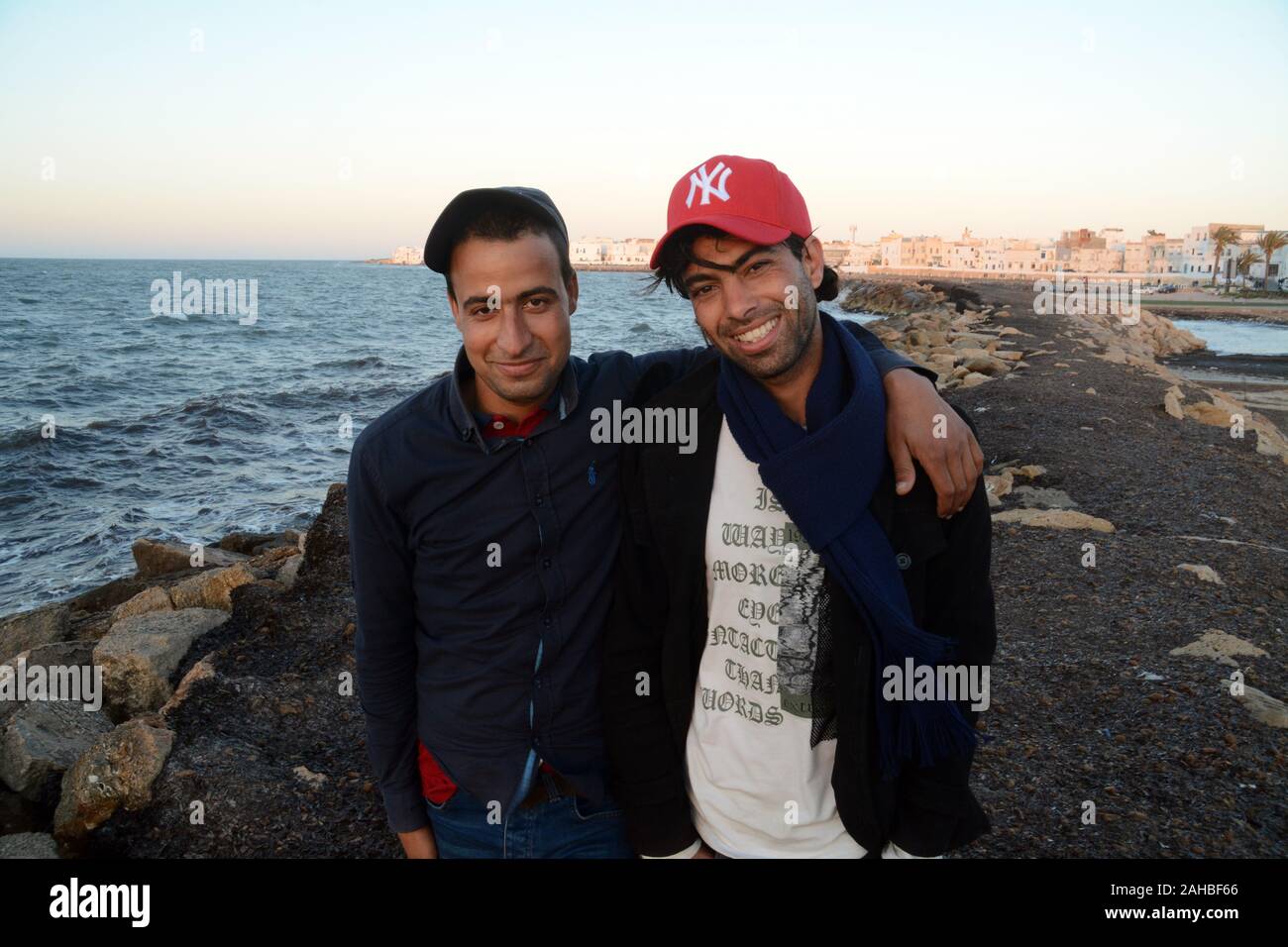 Zwei jungen tunesischen stehende Männer an der Küste in der Nähe der weiß getünchten Gebäude der Altstadt von Mahdia an der Mediterranen Küste von Tunesien. Stockfoto