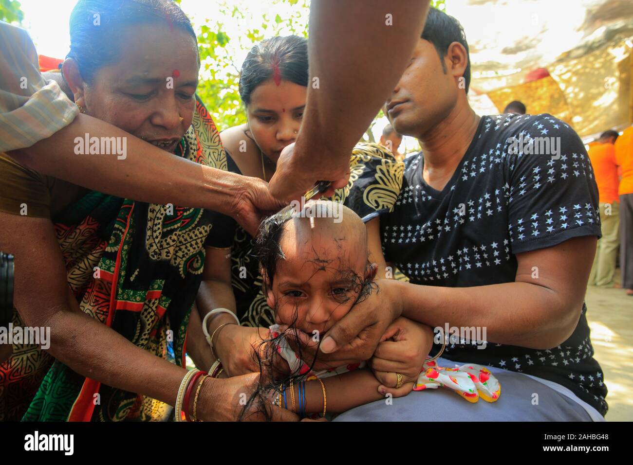 Mutter und Vater aufpassen der Friseur Scherkopf ihrer Tochter während der Bou Mela. Narayanganj, Bangladesch Stockfoto