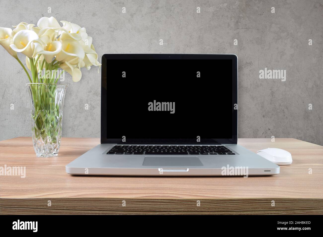 Moderner Laptop-Computer, der auf einem hellen Holzkaffeettisch mit einer Vase weißer Calla-Lilien ruht. Von Skandinavien inspirierte Betontexturwand. Stockfoto