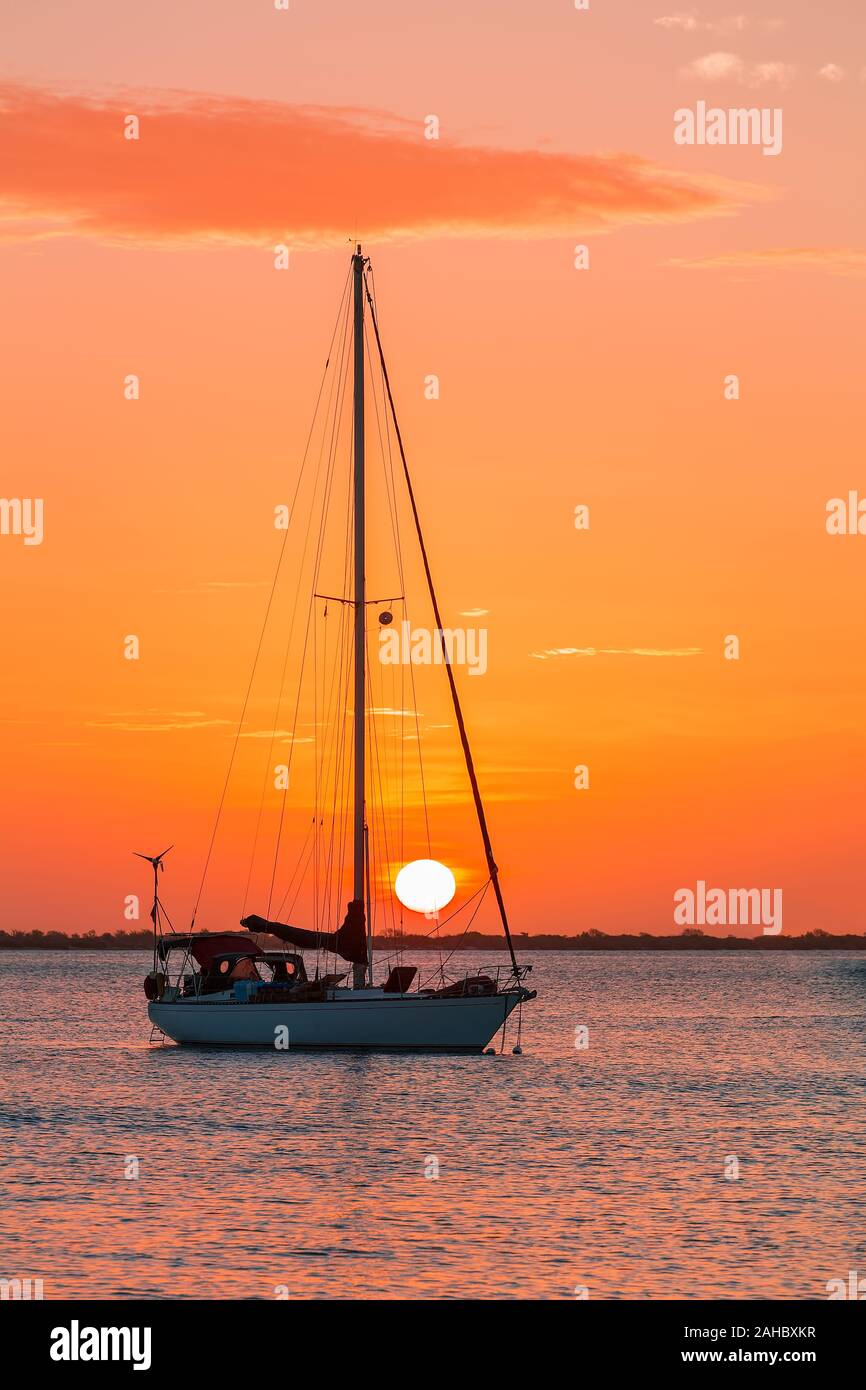 Ein einziges Segelboot auf das Meer bei der Einstellung Orange Sun Stockfoto
