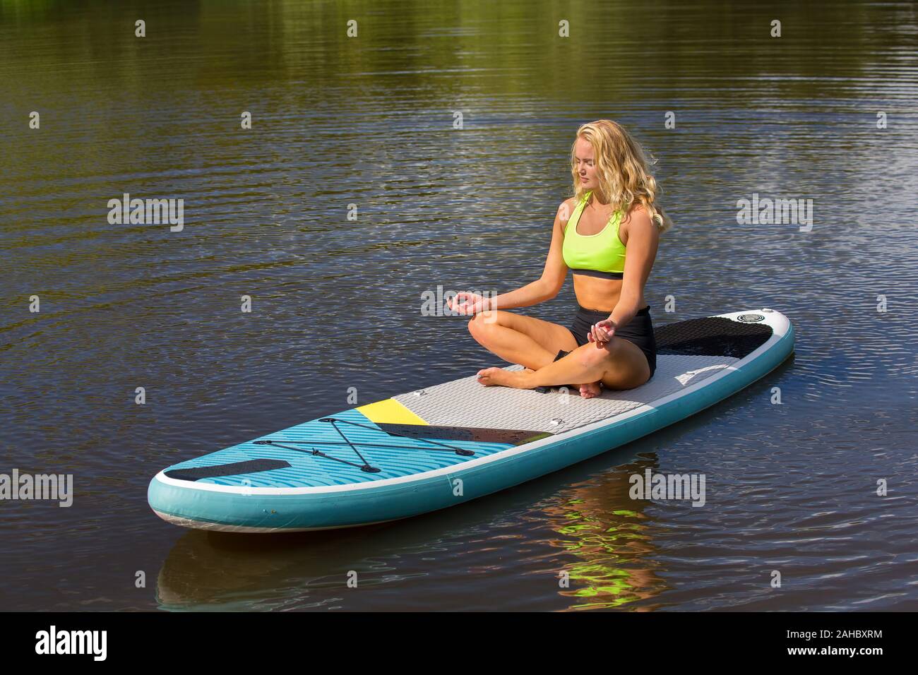 Junge europäische Frau meditiert auf SUP in niederländisch Fluss Stockfoto