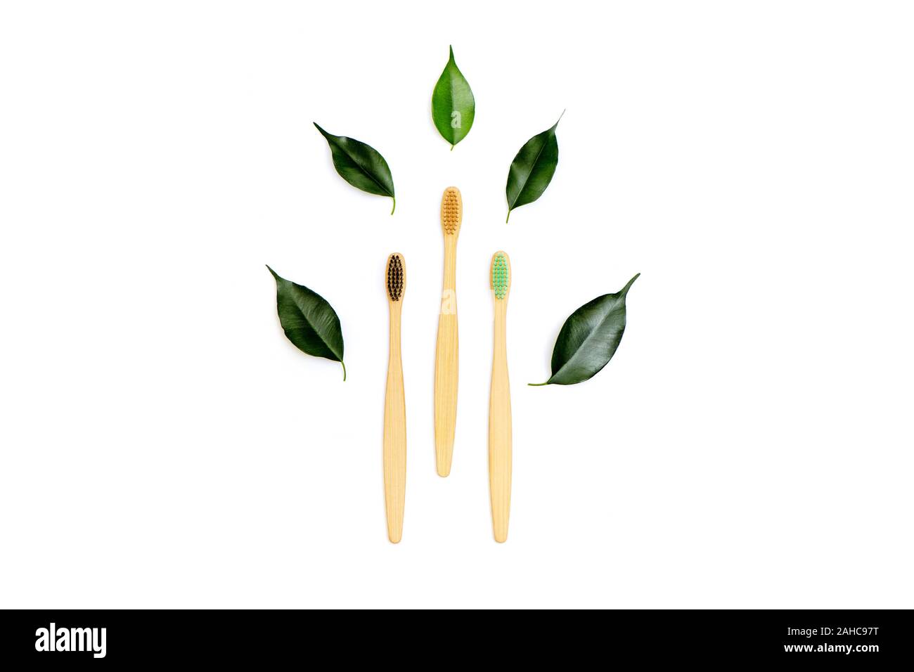 Menge der natürlichen Holz Bambus Zahnbürsten mit grünen Blättern auf weißem Hintergrund. Kunststoff Konzept. Stockfoto