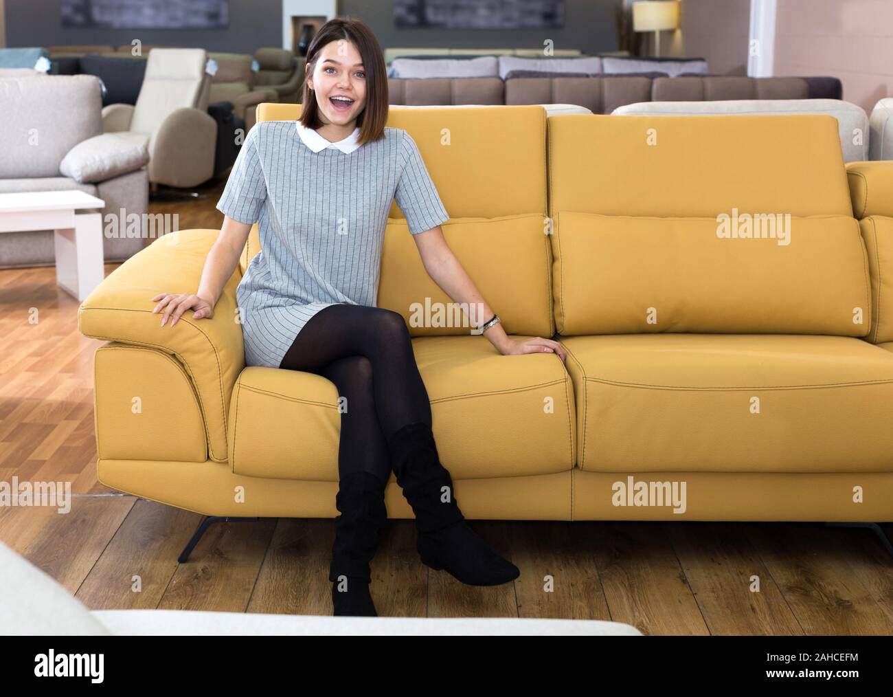 Porträt der jungen fröhliche Frau Prüfung gelb Sofa im Möbel Shop Stockfoto