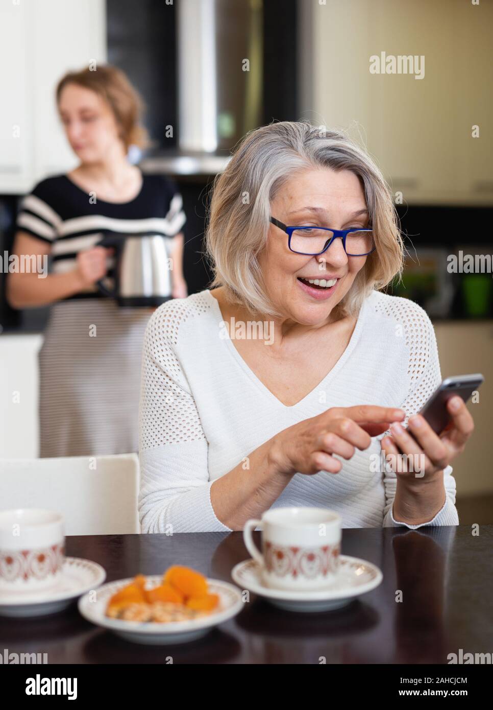 Positive ältere Frau mit Telefon, während junge Frau Tee Stockfoto