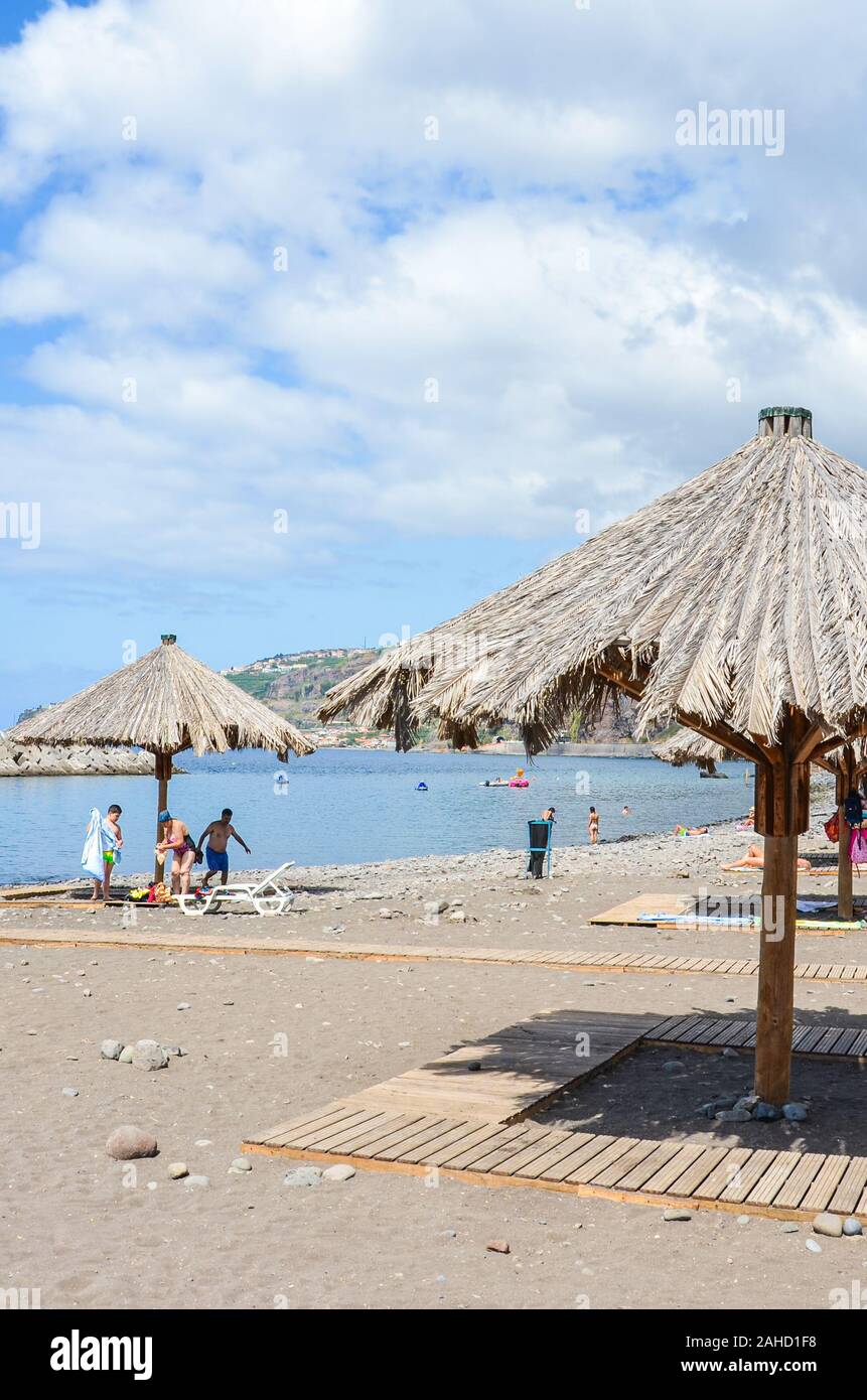 Ribeira Brava, Madeira, Portugal - Sep 9, 2019: Sandstrand im Madeira Reiseziel. Sonnenliegen und Sonnenschirmen, die Leute am Strand am Atlantischen Ozean. Sommertag. Vertikale Foto. Stockfoto