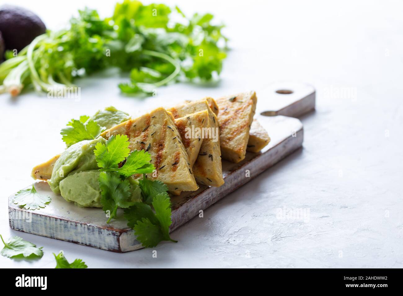Gegrillte herbed Tofu mit Avocadocreme, vegane Mahlzeit serviert auf rustikalen hölzernen Schneidebrett mit frischem Koriander Kräuter Stockfoto