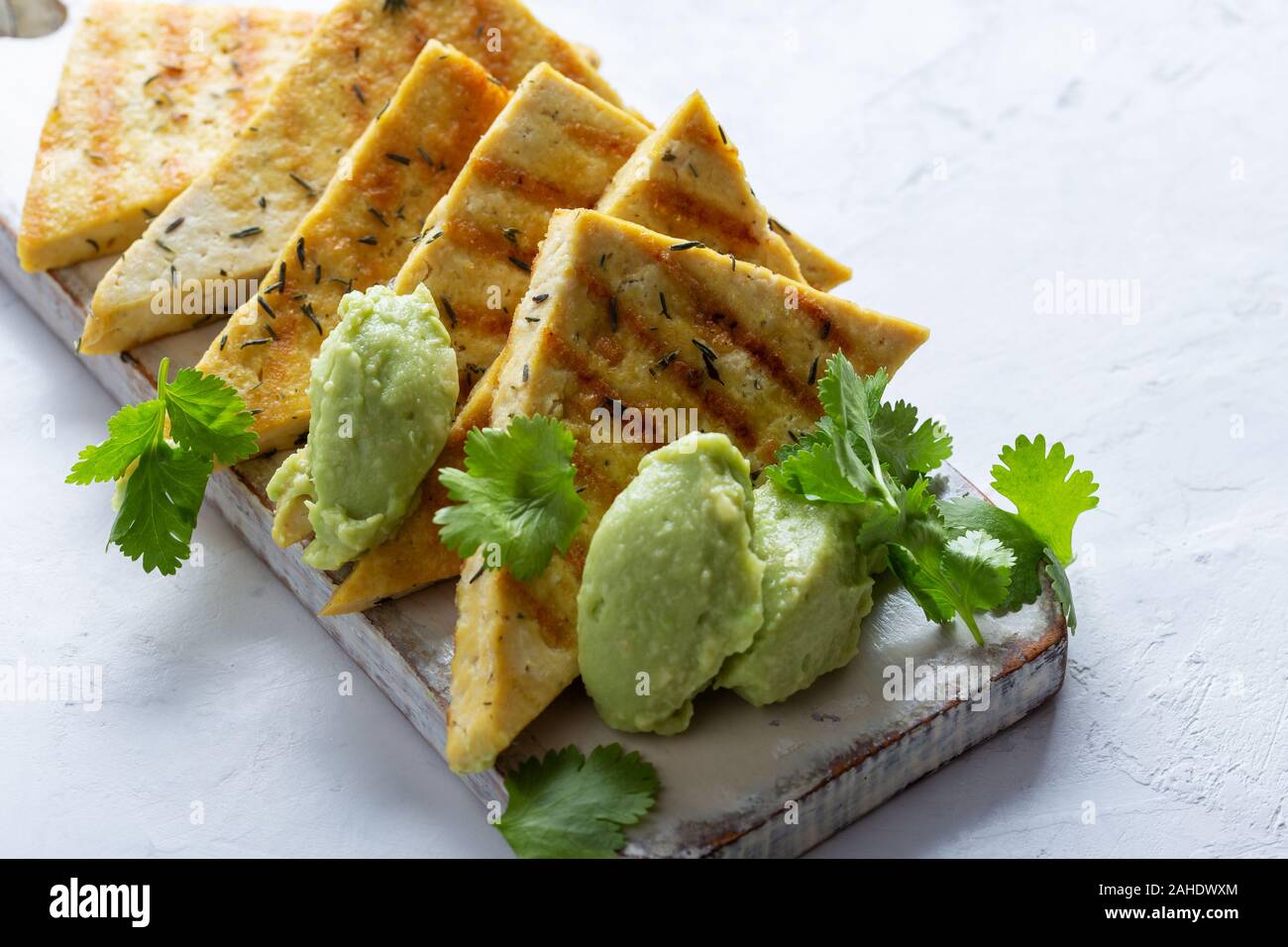 Gegrillte herbed Tofu mit Avocadocreme, vegane Mahlzeit serviert auf rustikalen hölzernen Schneidebrett mit frischem Koriander Kräuter Stockfoto