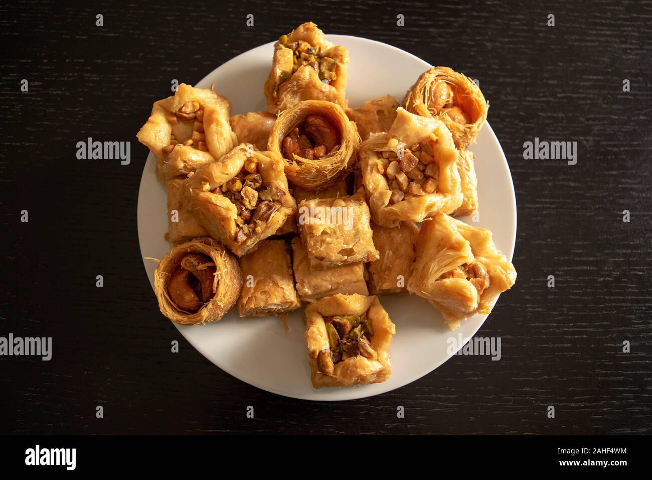 Traditionelle östliche sortierten Baklava. Ansicht von oben. Arabisch gebackene Süßigkeiten in weiße Platte auf dunklen Holztisch. Baklawa Mischung Stockfoto