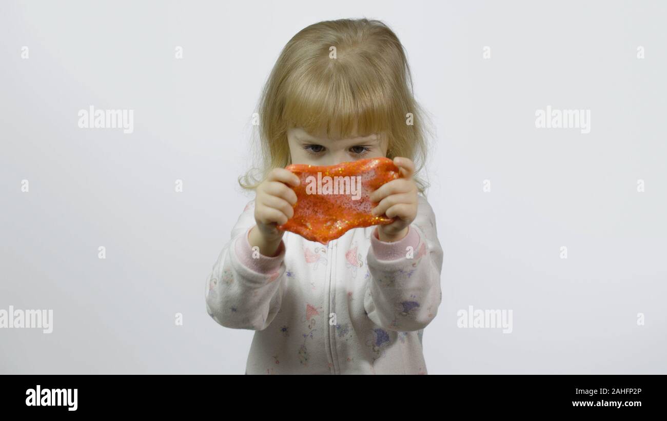 Kind Spaß machen orange Schleim. Kid spielen mit Hand gemacht Spielzeug Schleim. Lustig kind Mädchen. Entspannung und Zufriedenheit. Seltsamerweise zufriedenstellend orange Schleim für puren Spaß und Stress Relief. Weißer Hintergrund Stockfoto