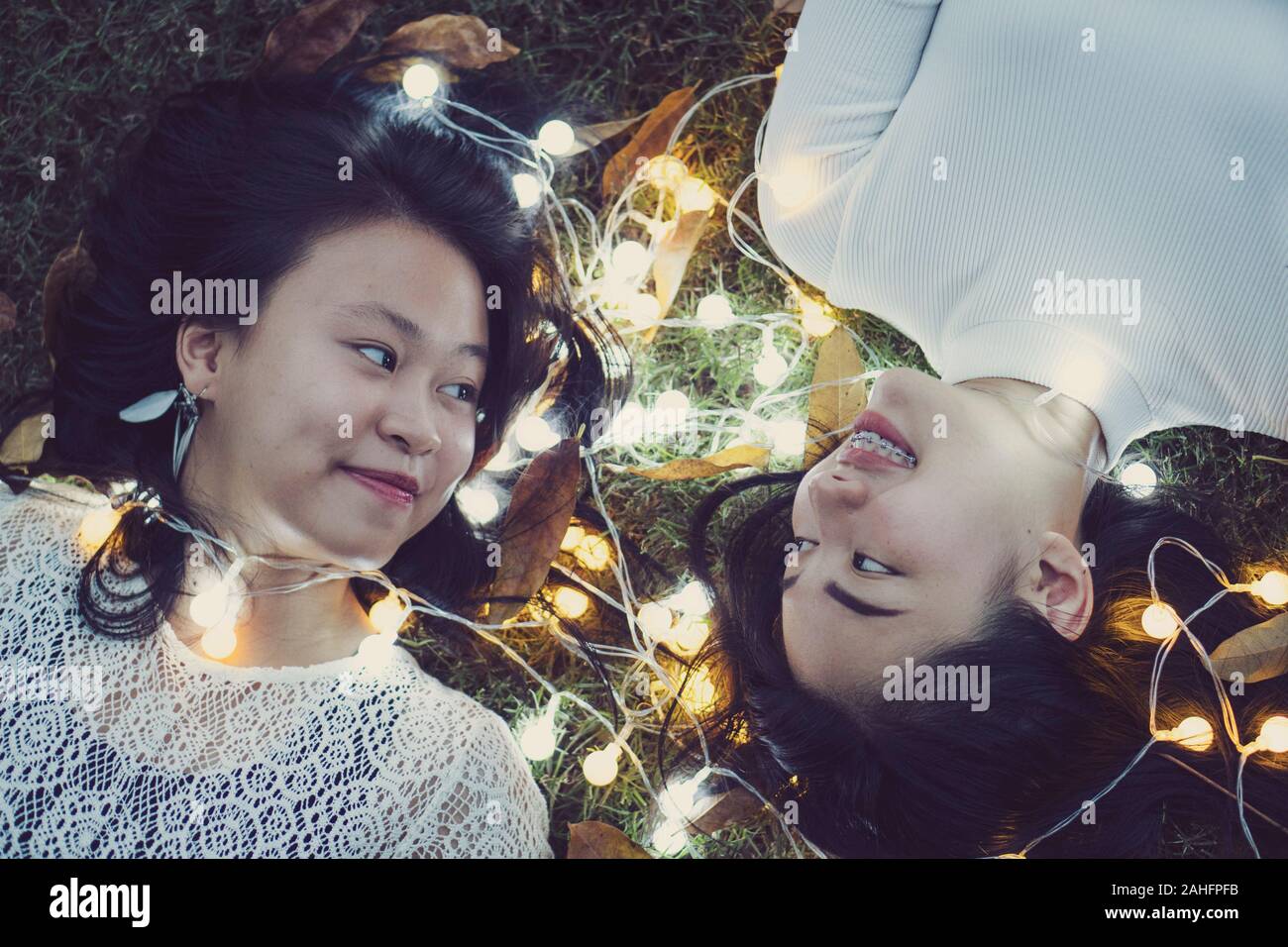 Zwei hübsche Mädchen beste Freunde liegen auf bunte Lichter auf dem Gras. Glückliche Freundschaft Konzept Stockfoto