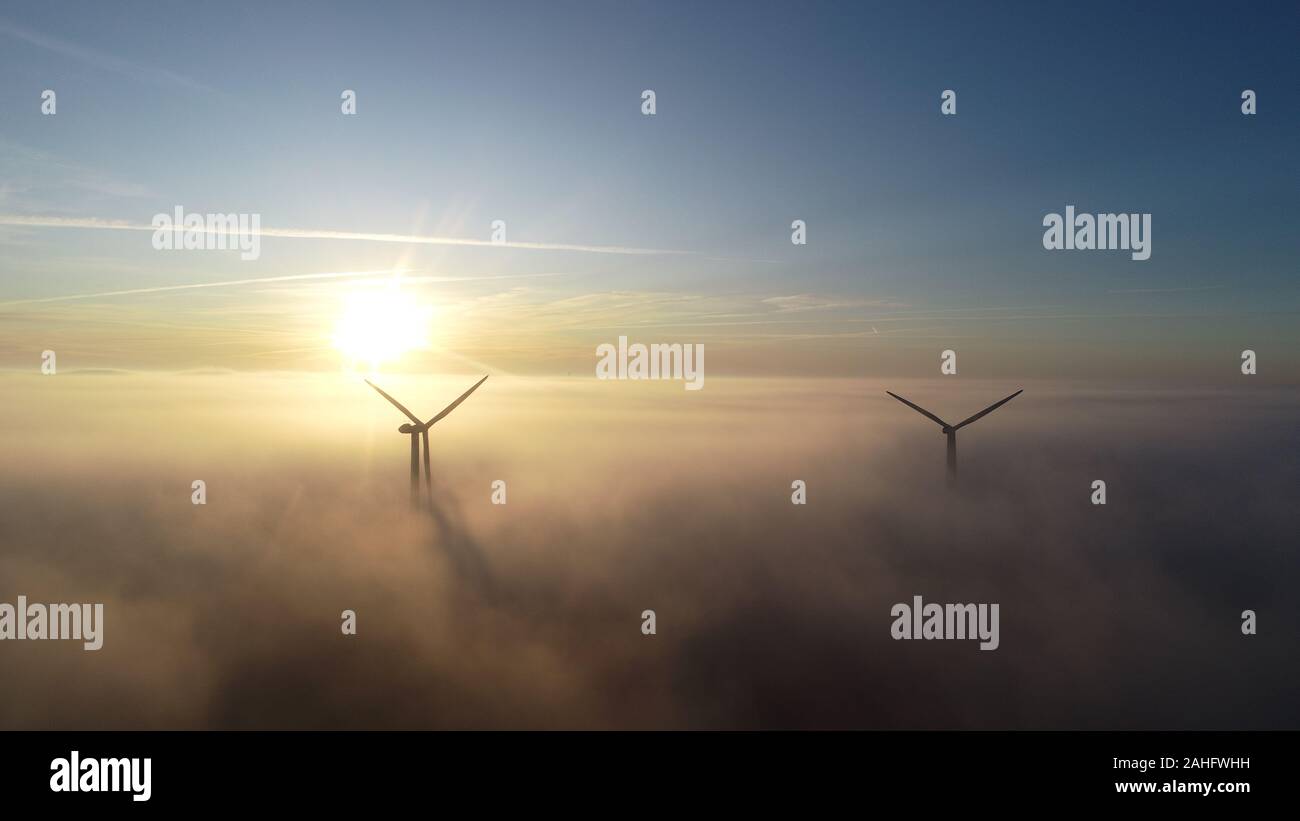 Luftbild von Windenergieanlagen bei Sonnenaufgang mit niedrigen Wolken/Nebel über dem Boden. Stockfoto